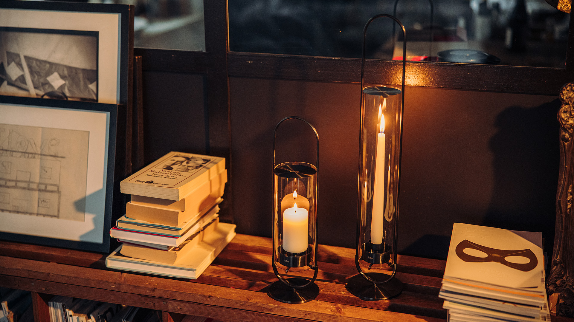 The 00273 Oval Candle 35 black integrates seamlessly into the setting, where a table with a candle, books and a picture.