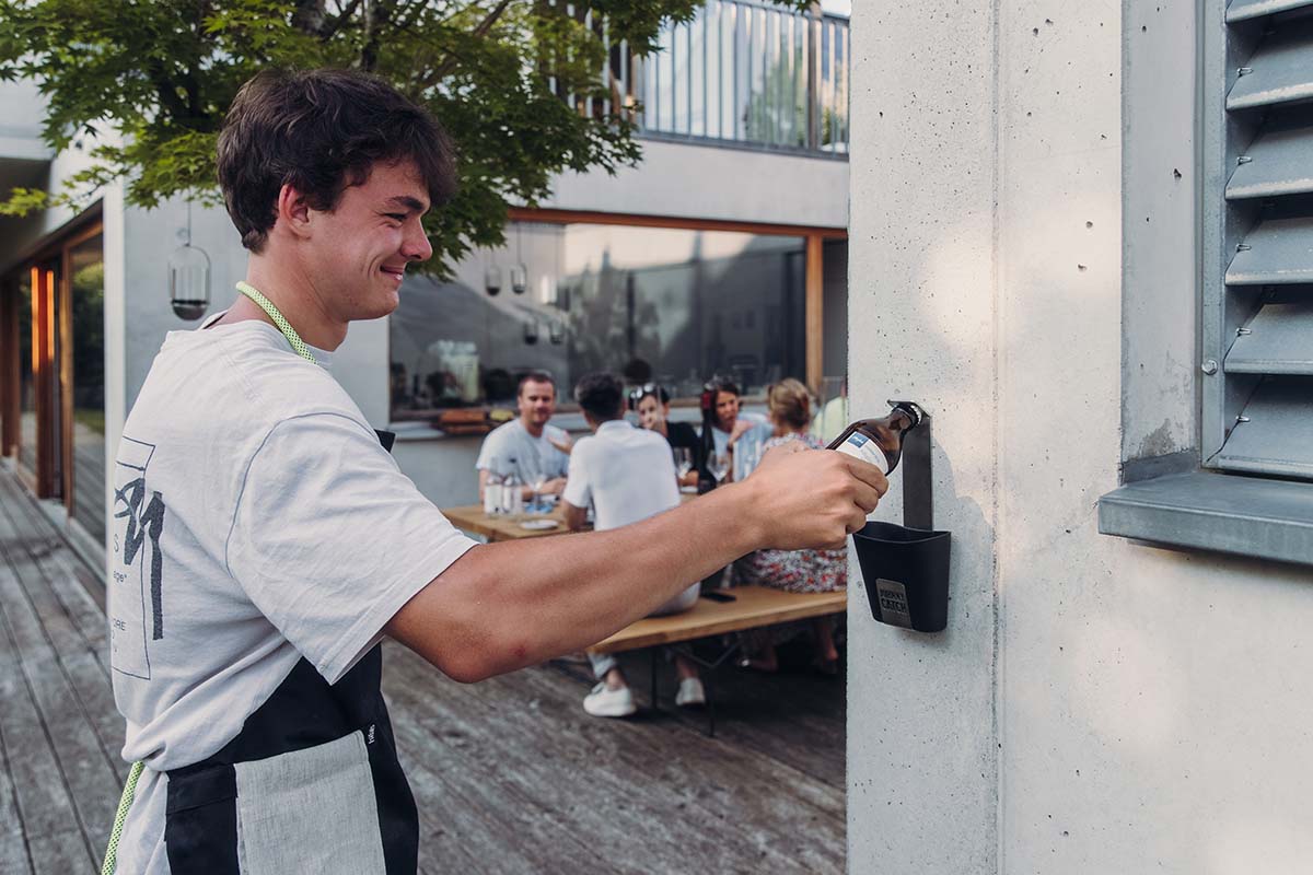 JOHNNY CATCH Cup Flaschenöffner silber Eine Darstellung eines Mannes, der in einem Restaurant eine Flasche öffnet, wobei der Johnny Catch Cup Flaschenöffner als zentrales und zweckmäßiges Element dient.