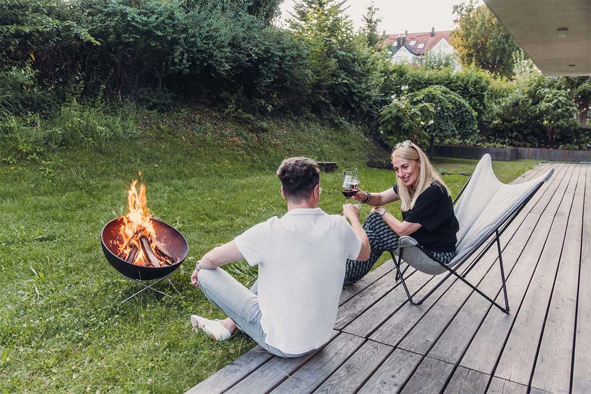 BOWL 57 Pied bas en étoile Une scène accueillante avec un homme et une femme assis sur un banc à côté d'un brasero, mise en valeur par la présence du BOWL 57 Pied bas en étoile.