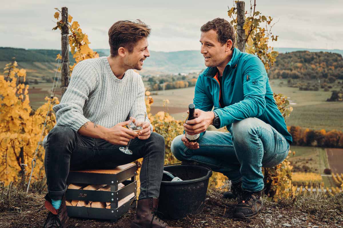 CRATE Feuerkorb Zwei Männer sitzen im Herbst auf einem Hügel, wobei der Crate Firebasket eine funktionale und elegante Note zur Szene hinzufügt.