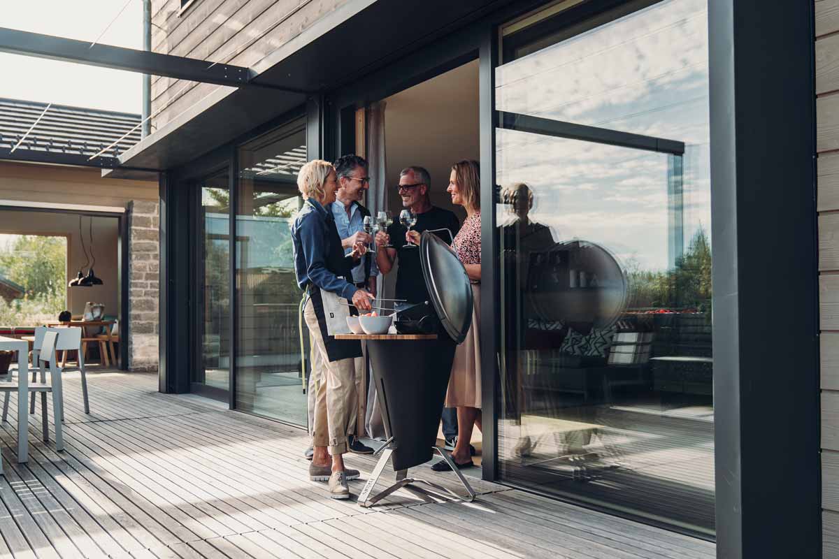 CONE Charcoal Grill The photo presents a couple standing on a deck looking at a tablet, with the CONE Charcoal Grill.