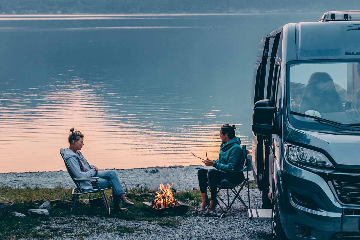 TRIPLE 65 Fire Bowl A view of a couple sitting around a camper van on a lake shore, with the TRIPLE 65 Fire Bowl.