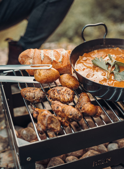 Eine Person kocht Essen auf einem Grill, der Crate Firebasket ergänzt den Moment mit seinem durchdachten Design.