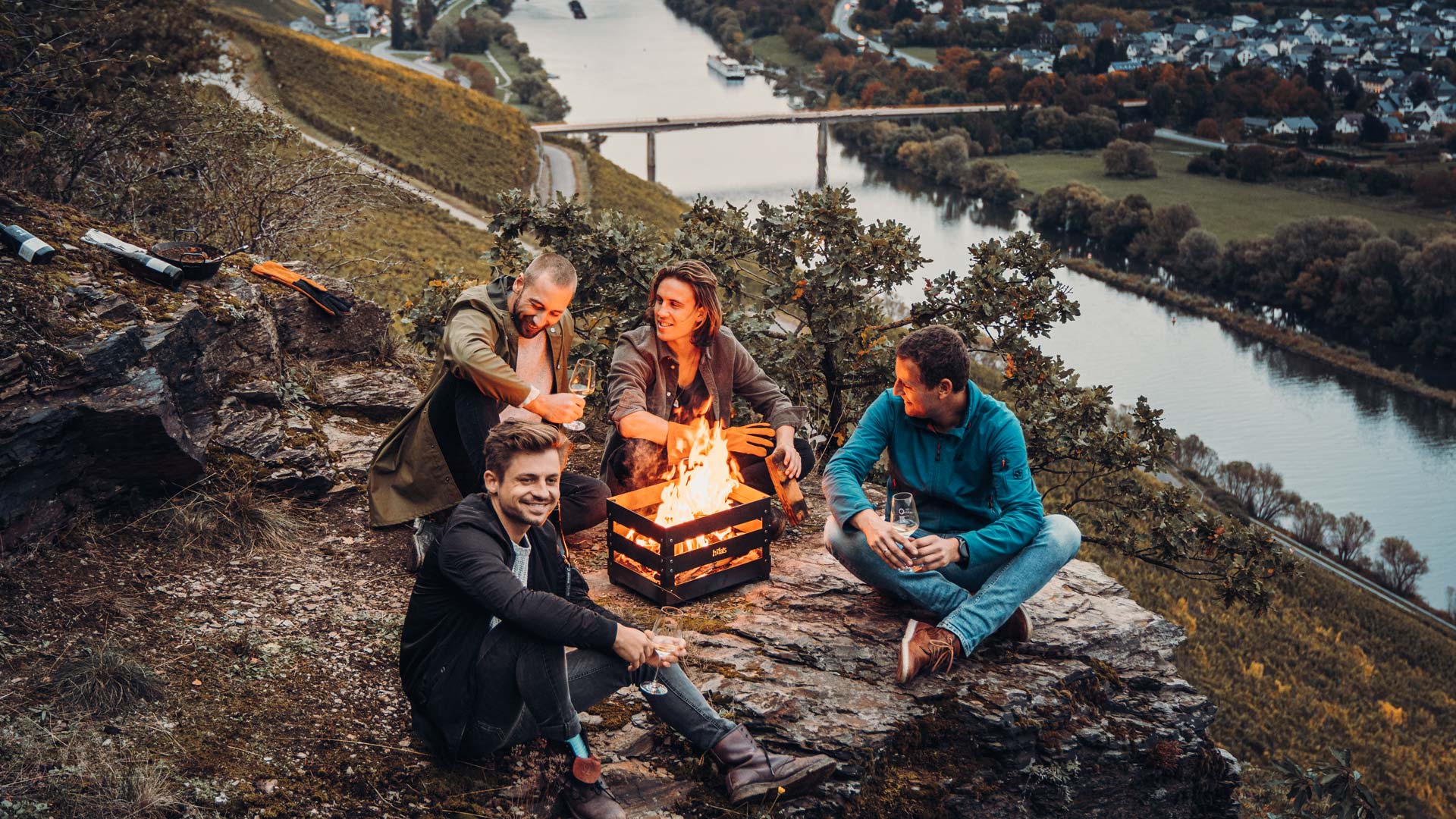 Erleben Sie drei Personen, die um ein Lagerfeuer sitzen, mit der eleganten Note des Crate Firebasket.