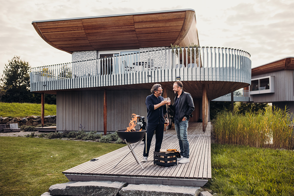 BOWL 57 Fire Bowl with tripod A man standing on a wooden deck, with the 00250 Bowl 57 with Tripod adding a functional and elegant touch to the scene.