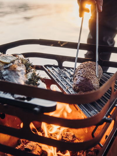 Een man grilt vlees op een grill, de Cube Firebasket met Plancha vult het moment aan met zijn doordachte ontwerp.