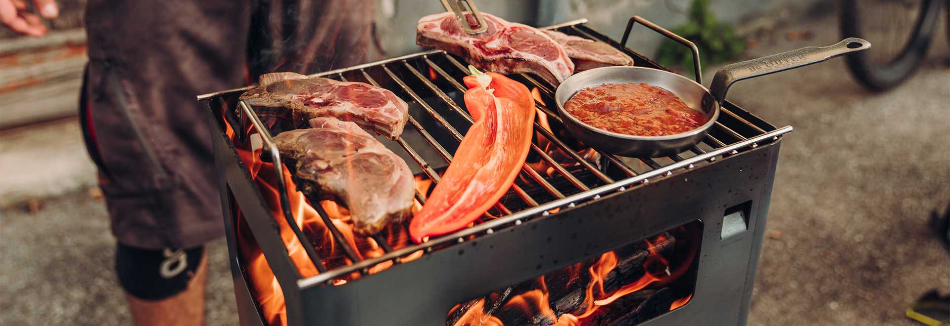 This image shows a man is cooking meat on a grill, with the BEER BOX Fire Basket.