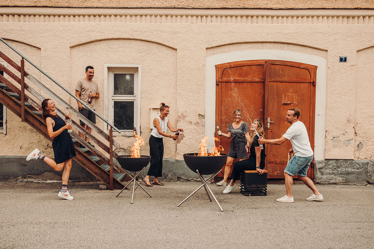 BOWL 70 Trépied La photo présente un groupe de personnes assises autour d'un brasero, avec le trépied BOWL 70.