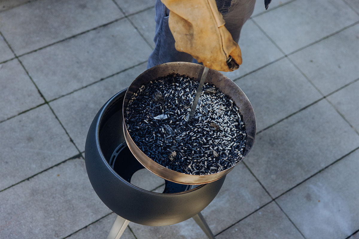 Das 00832 MOON 45 Erhöhung für Ascheschale wird als Person dargestellt, die eine Schale mit verbrannten Holzpellets hält, was ein stilvolles und zugängliches Bild ergibt.