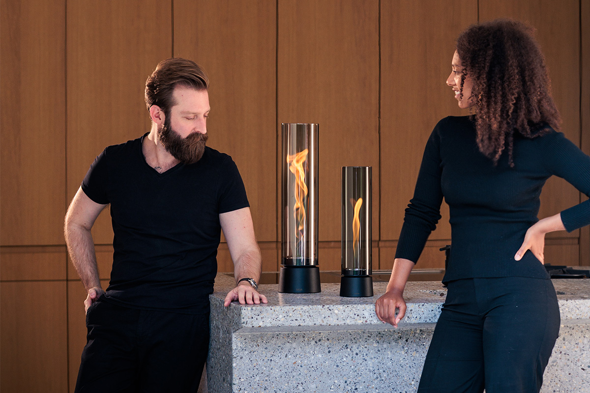 SPIN air 1200 Tischfeuer all black Zwei Personen lehen an Tisch und schauen in die Flamme von SPIN air 900 mattschwarz und SPIN air 1200 mattschwarz