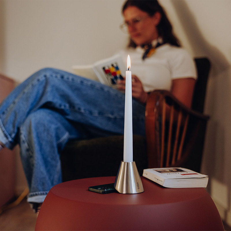 Digi Detox mit Smartphone darunter auf Beistelltisch. Im Hintergrund eine lesende Frau.