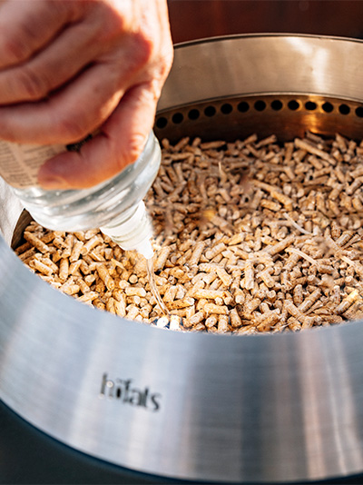 Scène waarin een persoon vloeibare ethanol op houtpellets in een grill giet, om te laten zien hoe je de MOON 45 aansteekt