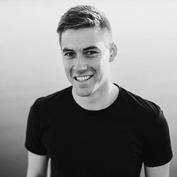 Ein Mann lächelt, während er vor einem See steht.