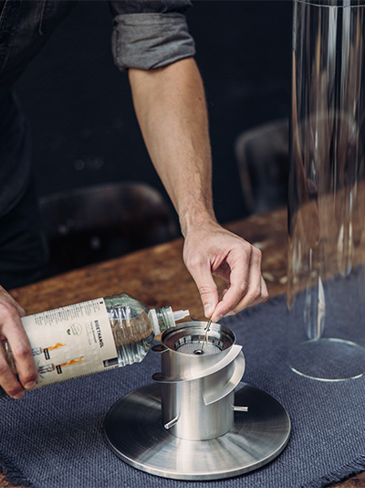 De Spin 1500 Staande Openhaard wordt getoond als een man die een drankje inschenkt, wat een stijlvol en toegankelijk beeld creëert.