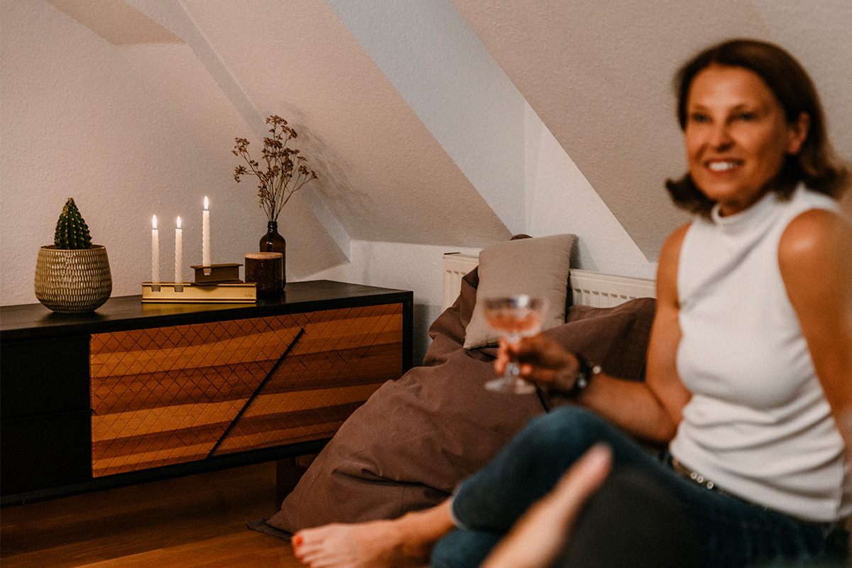 HENRY METAL I gold Szene, in der eine Frau auf einem Sofa sitzt und ein Glas Wein hält, wobei der 00662 Henry Metal II Gold durch seine praktische Eleganz hervorsticht.