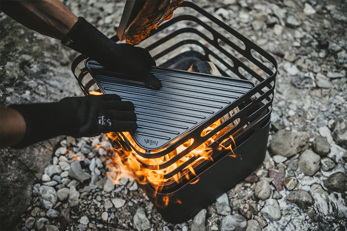 Feuerhandschuhe Aramid Szene, in der eine Person auf einem Grill kocht, wobei die 00715 Feuerhandschuhe Aramid durch ihre praktische Eleganz hervorstechen.