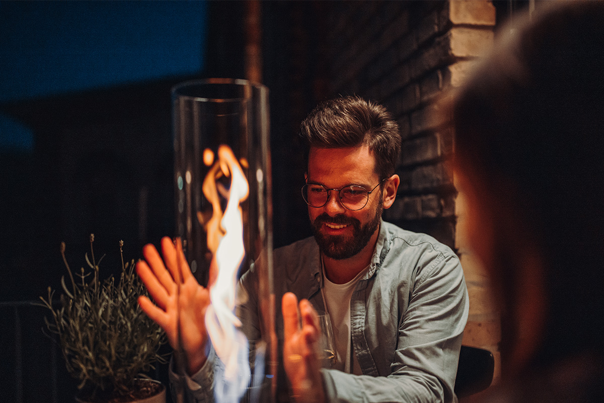 SPIN 120 Tabletop Fireplace silver A depiction of a man is smiling while he looks at a fire, featuring the Spin 90 Tablefire silver as a central and purposeful element.