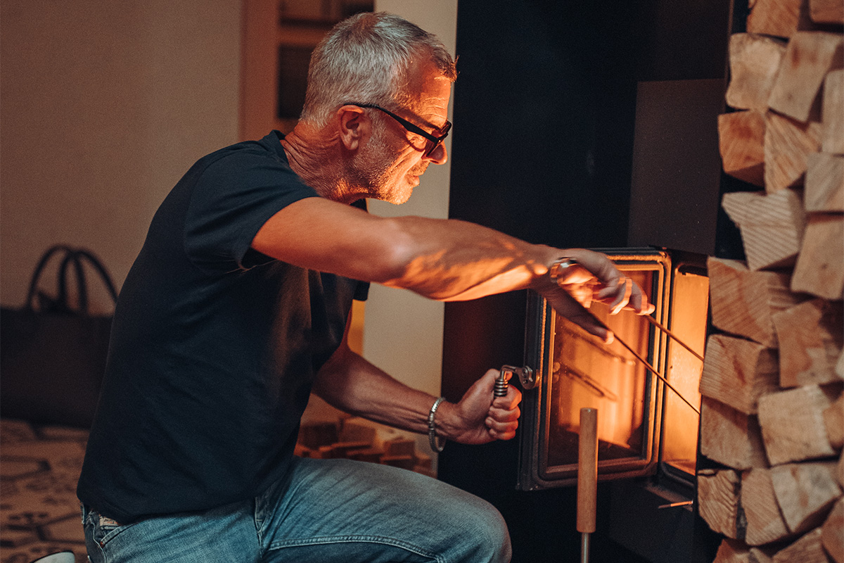 Feuerzange Auf dem Bild ist ein Mann zu sehen, der ein Feuer im Holzofen anzündet, mit der Feuerzange.