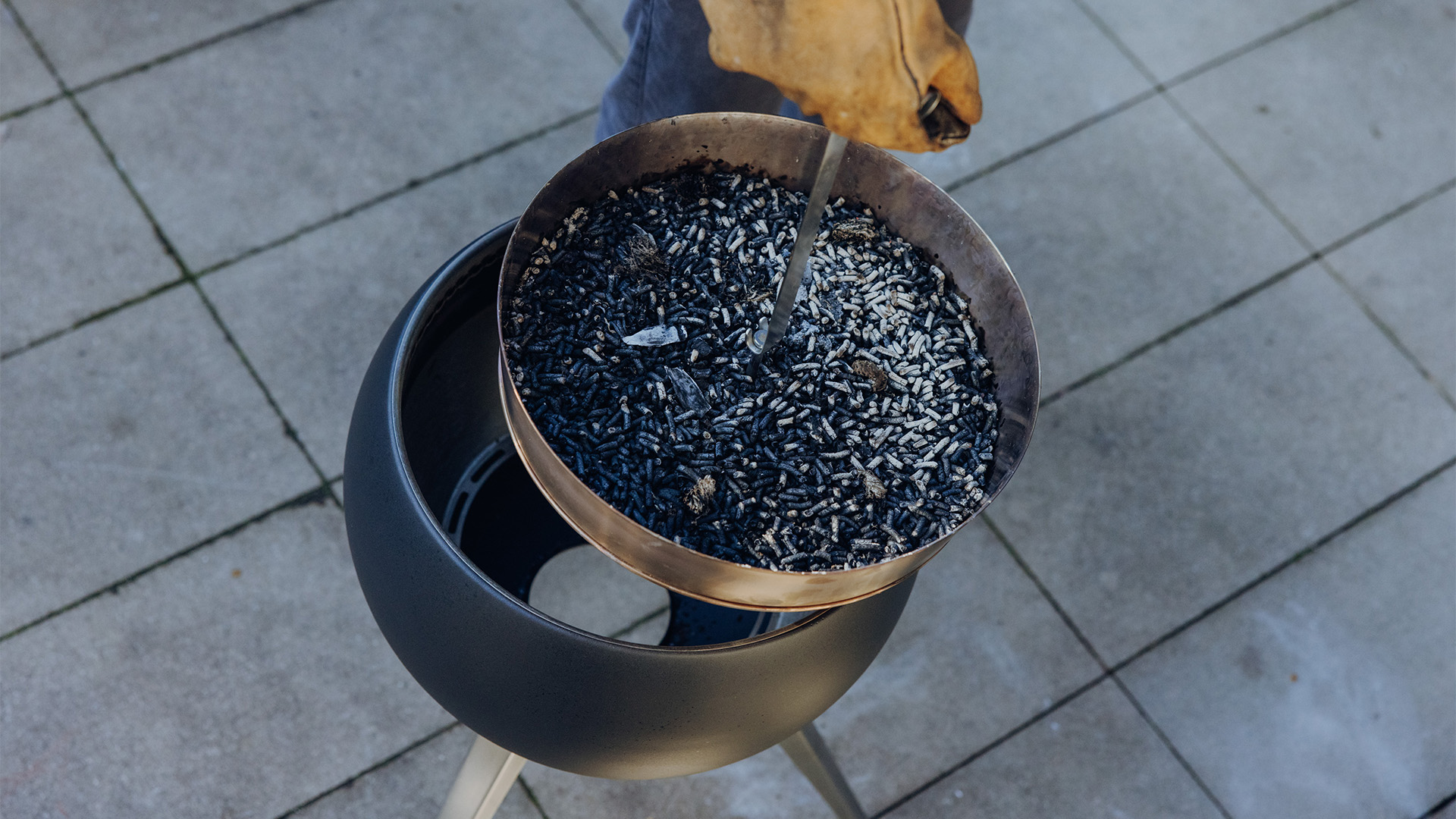 Das 00832 MOON 45 Erhöhung für Ascheschale wird als Person dargestellt, die eine Schale mit verbrannten Holzpellets hält, was ein stilvolles und zugängliches Bild ergibt.