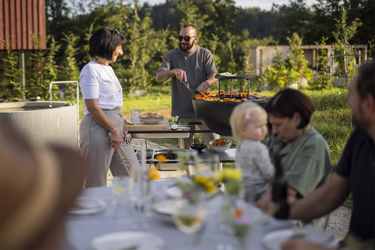 FIRE KITCHEN mit BOWL 70 Plancha-Grillset tief Das 00740 Fire Kitchen Bowl 70 Plancha BBQ Set wird als Gruppe von Personen gezeigt, die um einen Tisch sitzen und ein stilvolles und zugängliches Bild schaffen.
