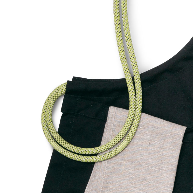 Schürze Dieses Bild zeigt eine schwarz-weiße Schürze mit einem grünen Band, mit dem Flyer TOOLS.