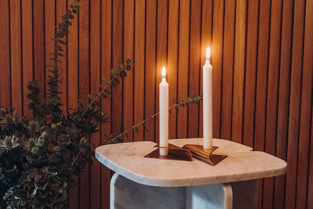 This image shows a candle and a book on a table, with the SQUARE CANDLE Candleholder gold.