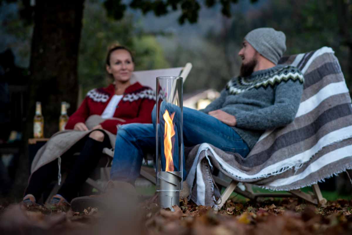 SPIN 1200 Stand Elevation silver Scene showing a man and woman sitting on a blanket around a fire, where the Spin 120 stand elevation silver stands out for its practical elegance.