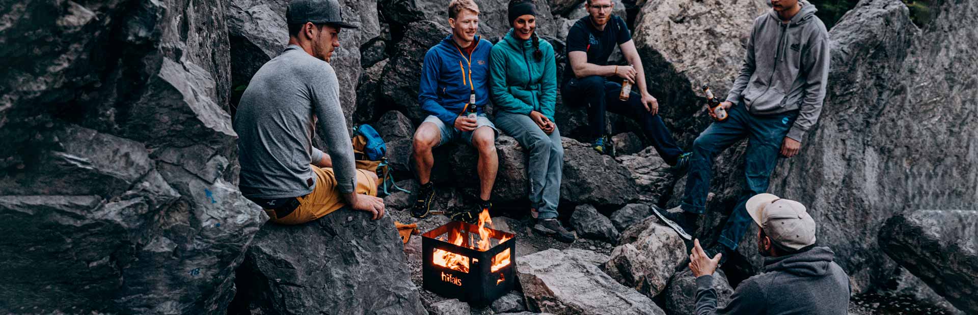 Ein Bild, das eine Gruppe von Menschen zeigt, die um ein Lagerfeuer sitzen, mit dem BEER BOX Feuerkorb.