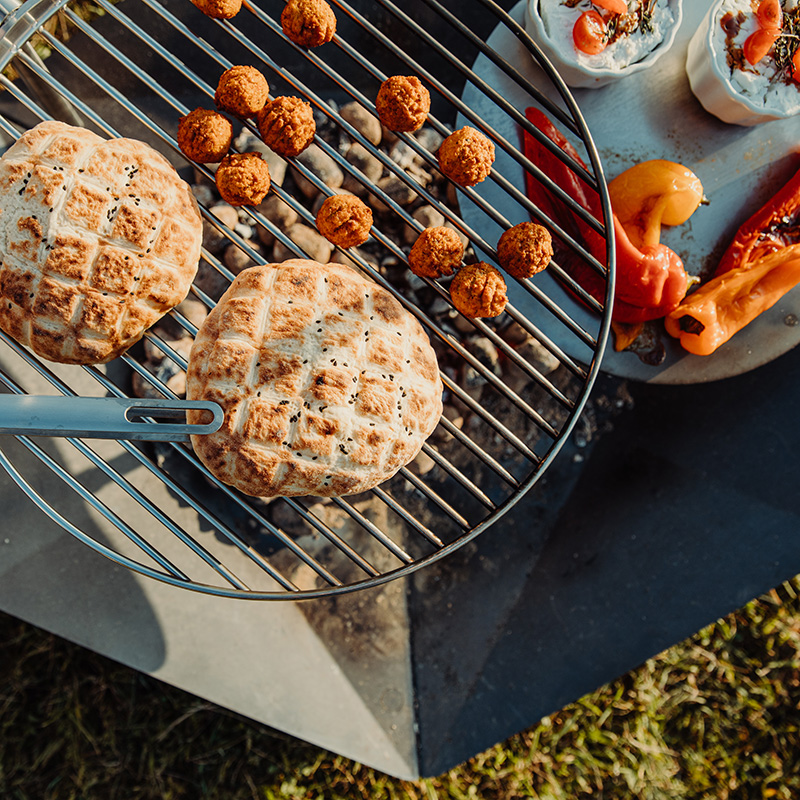 Scène montrant un barbecue avec de la nourriture dessus, où le TRIPLE Fireplace se distingue par son élégance pratique.