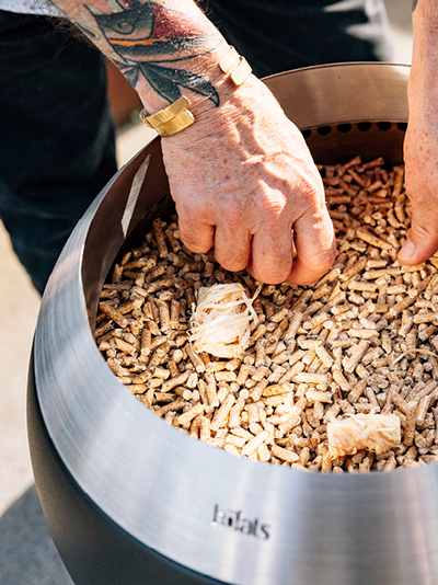 A person is putting wooden chips into a fire basket. Showing how to light the MOON 45
