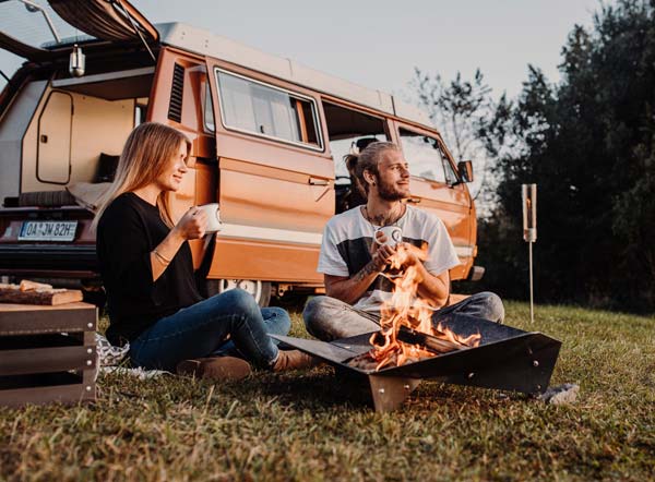 a couple sitting on the grass next to a camper van