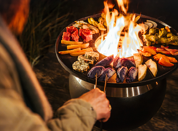 a person is grilling on the MOON Plancha holding vegetables with a tong.