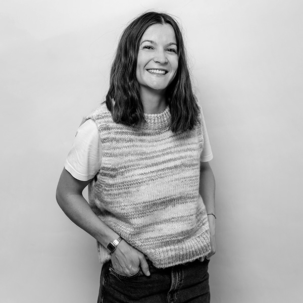 Eine Frau in einem Pullover und Jeans steht an einer Wand.