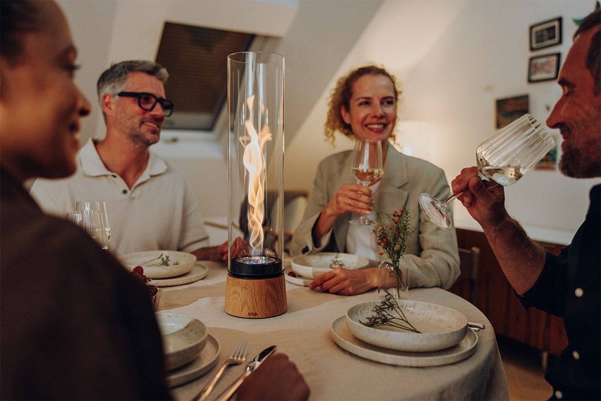 SPIN air 1200 Tischfeuer Eiche SPIN air 1200 Tischfeuer Eiche an einem runden gedeckten Tisch und vier Menschen sitzen um das Tischfeuer