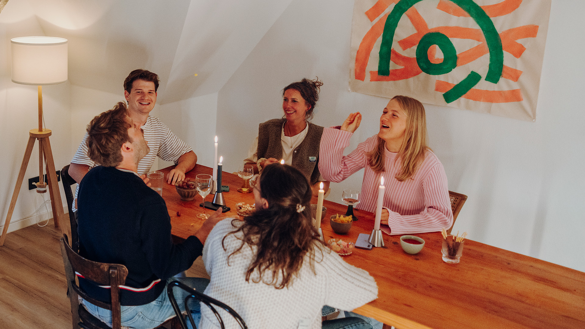 Fünf Personen sitzen ins Gespräch vertieft an Esstisch. Dabei liegen die Smartphones jeweils unter einem Digi Detox Kerzenhalter.