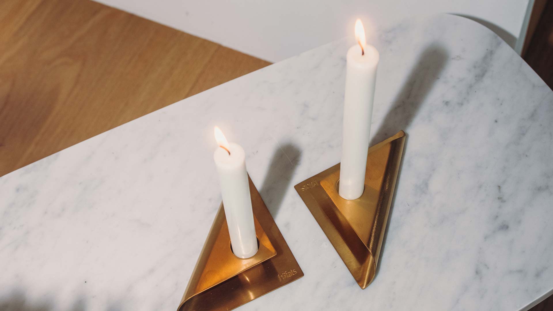 Scene showing two candles on a marble table, where the Square Candle Candleholder Gold stands out for its practical elegance.