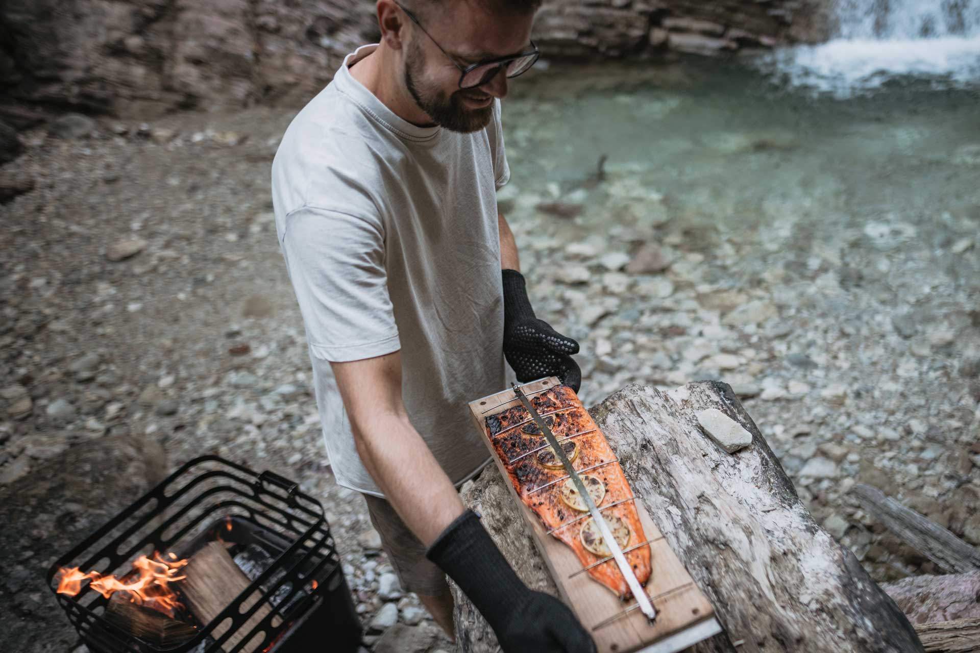 Ein Mann kocht über einem Lagerfeuer, wobei das Cube Ocean Set eine funktionale und elegante Note zur Szene hinzufügt.