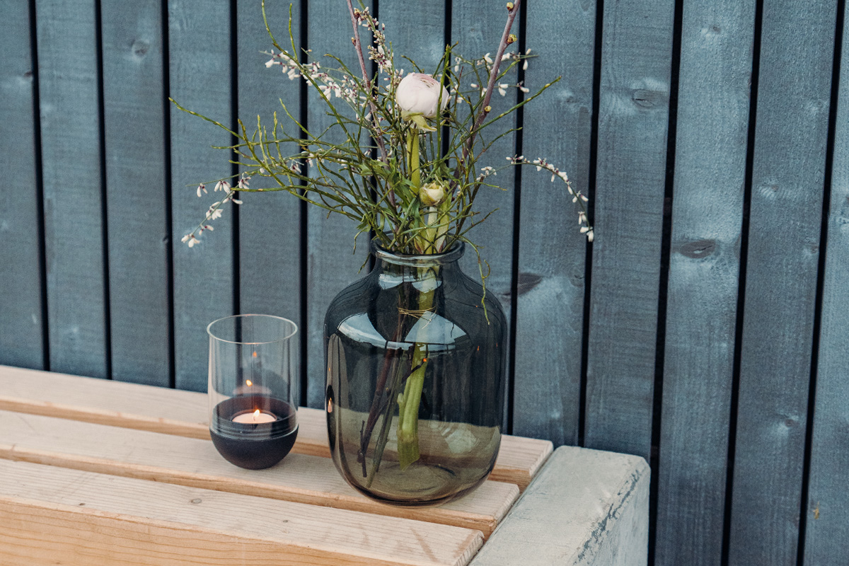 GRAVITY CANDLE Lantern black The 00544 Gravity Candle black integrates seamlessly into the setting, where a vase with flowers and a candle on a wooden table.