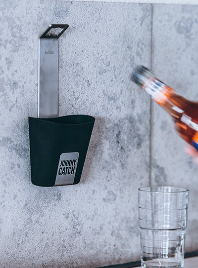 Eine Flasche Alkohol wird in ein Glas gegossen, bereichert durch die Anwesenheit des Johnny Catch Cup Flaschenöffners, der Design mit Nutzen verbindet.