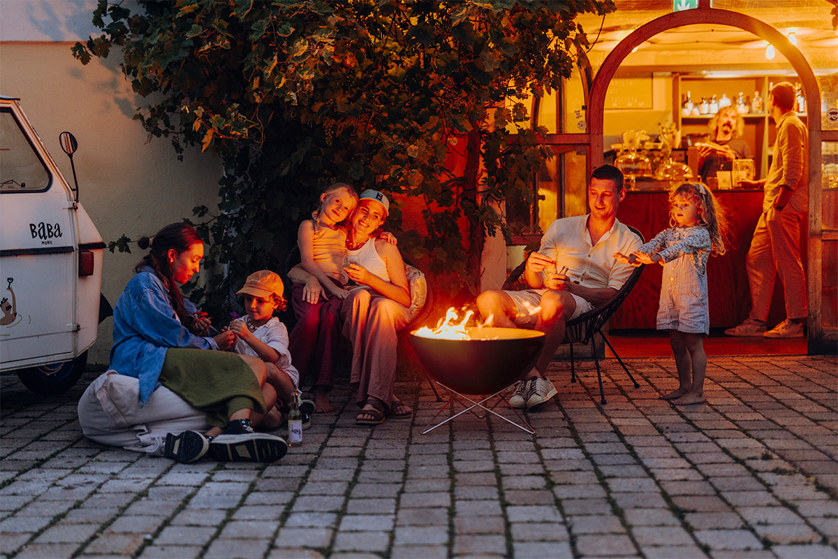 BOWL 57 Feuerschale mit Sternfuß Szene, die eine Gruppe von Menschen zeigt, die um eine Feuerstelle sitzen, wobei die Bowl 57 mit Sternständer durch ihre praktische Eleganz hervorsticht.