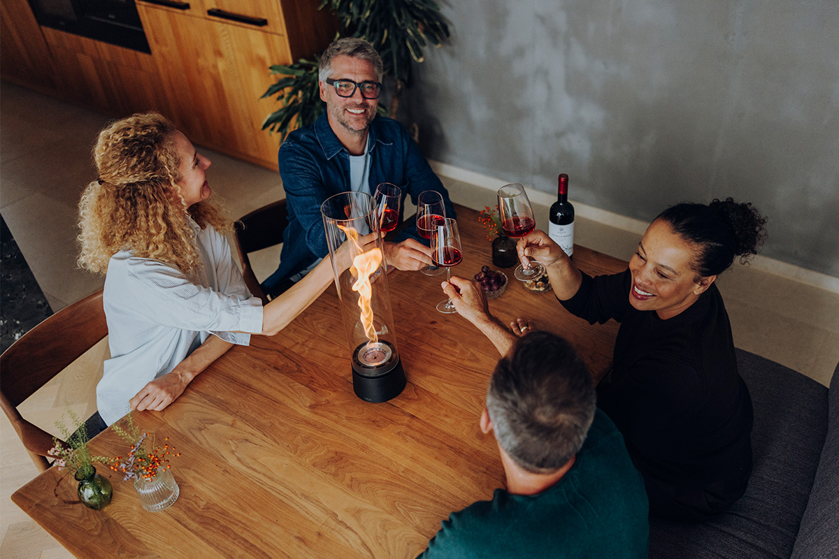 SPIN air 1200 Tischfeuer mattschwarz SPIN air 1200 und 900 mattschwarz auf einem Küchentisch mit vier Personen welche mit einem Rotwein anstoßen