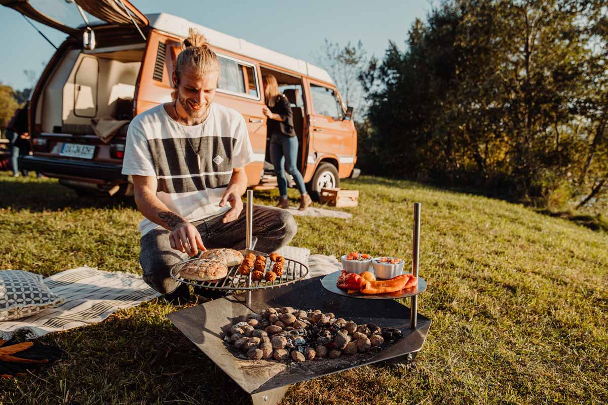 TRIPLE Grille 45 Scène montrant un homme assis sur l'herbe devant un camping-car, où le TRIPLE Grille 45 se distingue par son élégance pratique.